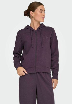 Vijolična zip-up kapuca iz mehkega materiala. Ima kapuco, sprednje žepke in minimalno blagovno znamko na prsih.