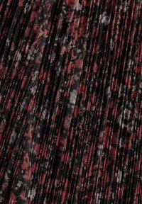 Tissu noir transparent avec imprimé floral rouge, blanc et marron et plis verticaux serrés créant texture et profondeur.