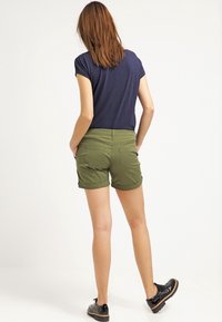 Olijfgroene shorts met opgerolde manchetten, gemaakt van lichtgewicht stof. Voorzien van achterzakken en gedragen met een marineblauwe t-shirt en zwarte schoenen.
