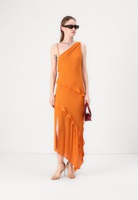 Asymmetrisk orange klänning med volangdetaljer, en hög slits vid låret och tunna axelband. Bärs med nya högklackade skor i nude och en liten röd handväska.