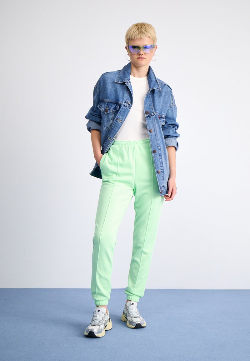 Jeansjacke, weißes Hemd, mintgrüne Sweatpants und silberne Sneakers. Als Accessoires dienen blau getönte Sonnenbrillen und übergroße Creolen.