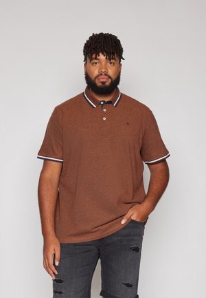 Brun kortærmet polo skjorte med en marineblå krave og hvide striber. Stoffet ser tekstureret ud, parret med mørke slidte denim shorts.