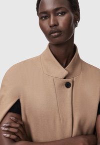 Cappotto in misto lana color corda con colletto alto, chiusura a un bottone nero e maniche corte, caratterizzato da una texture liscia e un design strutturato.