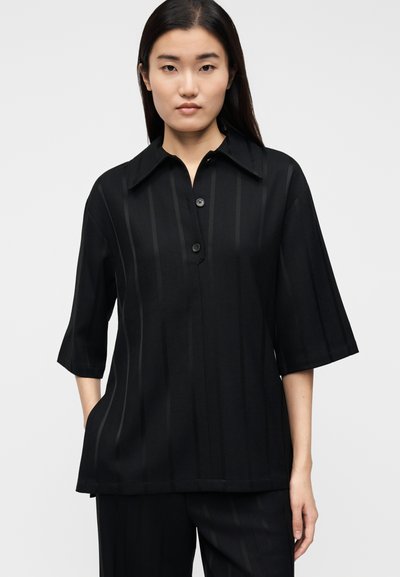 Camicia nera a maniche corte con colletto appuntito, caratterizzata da sottili righe verticali e chiusura frontale con bottoni. Tessuto liscio con vestibilità comoda.