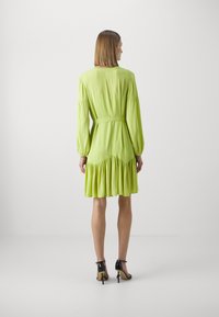 Lime green dress with long sleeves, cinched waist, and ruffled hem. Smooth texture, lightweight fabric, and a fitted silhouette highlight design.