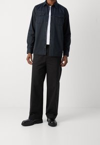 Dunkelblaues Hemd mit Knopfleiste und zwei Brusttaschen, kombiniert mit schwarzen weiten Hosen und schwarzen klobigen Stiefeln. Glatte Textur, lässiges Design.