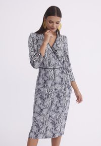 Czarna i biała sukienka o wzorze węża, zapinana na krzyż, z rękawami trzyczwartowymi, dekoltem w serek oraz guzikami na rękawach. Miękka, teksturowana tkanina.