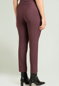 Pantalones burdeos de talle alto con un corte entallado, confeccionados en tela suave y con costuras sutiles, combinados con botines negros de punta afilada.