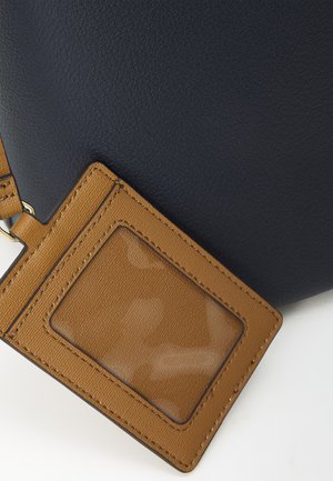 Navy leather bag with textured surface, featuring a rectangular tan ID card holder attached by a strap. Clear plastic window for visibility.