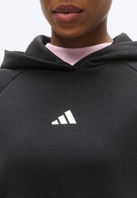 Μαύρο φούτερ με κουκούλα από βαμβακερό μείγμα ύφασμα με ροζ λαιμόκοψη. Διαθέτει λευκό λογότυπο με τρεις ρίγες στο στήθος, που τονίζει το μοντέρνο σχεδιασμό.