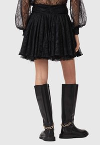 Jupe en dentelle noire et tulle avec un design plissé, associée à des bottes en cuir noir montantes ornées d'un accent en chaîne dorée.