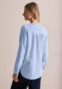 Camicia azzurro chiaro a maniche lunghe con orlo arrotondato, polsini abbottonati e yoke posteriore plissettato. Realizzata in un morbido tessuto testurizzato.