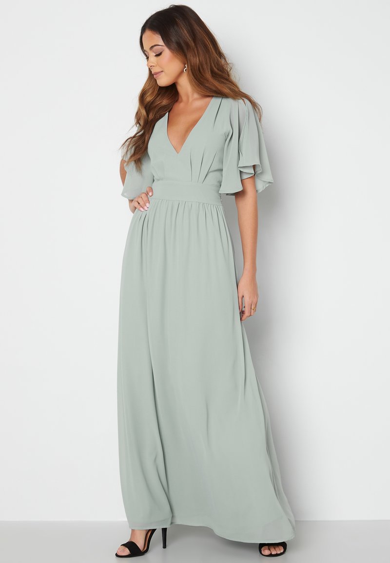 Langes, fließendes Kleid aus weichem grünem Stoff. Hat einen tiefen V-Ausschnitt, flatternde Ärmel und eine taillierte Taille. Bodenlang mit einer lockeren Silhouette.