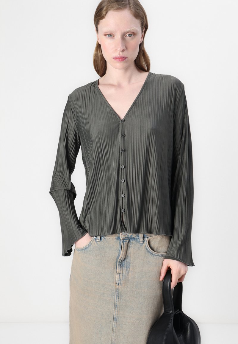 Dunkelgrüne, strukturierte Bluse mit V-Ausschnitt und langen Ärmeln. Verfügt über einen Knopfverschluss und wird mit einem hellen Jeansrock kombiniert.