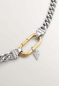 Pulsera de cadena de plata con un cierre ovalado dorado y un pequeño charm con la letra "F" incrustada de diamantes. Acabado metálico suave.