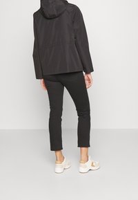 Czarna wodoodporna kurtka z kapturem, dopasowany fason i gładka tekstura. Połączona z czarnymi, wąskimi spodniami i białymi sportowymi butami z beżowymi akcentami.