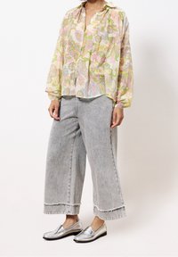 Blouse légère à motif floral aux couleurs pastel, associée à un jean gris délavé à jambes larges et des mocassins argentés brillants.