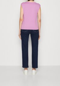 Fialový top s krátkými rukávy, který je spárován s tmavě modrými rovnými džíny a bílými teniskami. Hladká tkanina s jednoduchým, bezšvovým designem.