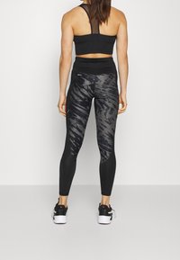 Czarny stanik sportowy z siateczkowymi detalami, w połączeniu z legginsami o wysokim stanie z wzorem w paski tygrysa w odcieniach szarości i czerni.