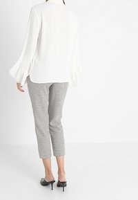 Blusa bianca a maniche lunghe con polsini svasati, abbinata a pantaloni cropped a scacchi in bianco e nero. Tacchi neri open-toe completano l'outfit.