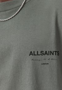 Camiseta de color verde oliva hecha de algodón, con cuello redondo acanalado y texto impreso en negro: "ALLSAINTS" con una firma y "LONDRES" debajo.