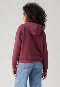 Burgundy-hoodie med avslappnad passform, ribbad mudd och nederkant. Kombineras med ljusblå, vida denimjeans.