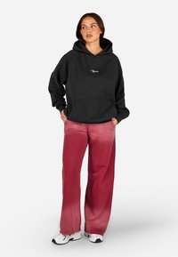 Čierna prehnaná mikina s predným vreckom, v kombinácii s ružovými ombré širokými nohavicami, doplnené bielymi športovými topánkami.