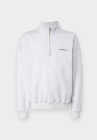Sudadera de color gris claro con cuello de media cremallera, puños y cinturilla acanalados. Presenta un logo negro en el lado izquierdo del pecho. Textura de tela suave.