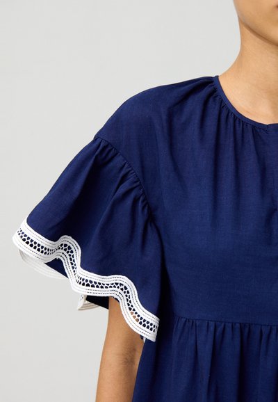 Vestido azul marino con mangas cortas acampanadas que presentan un borde de encaje blanco. Tejido ligero, por debajo del hombro, con un detalle de cintura fruncida.