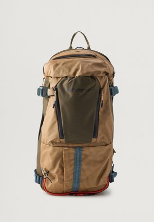 Mochila con una combinación de colores marrón claro y oliva, tejido texturizado, varios bolsillos, correas ajustables y un acento rojo en la parte inferior.