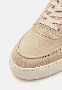 Baskets en suède beige avec un bout rond, une tige texturée et des lacets plats. Elles possèdent une semelle en caoutchouc blanche et de subtils accents cousus.