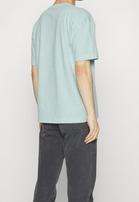 Mentově zelené tričko s krátkým rukávem a kulatým výstřihem, volného střihu, lehkého materiálu a rovného lemu, spárované s tmavě šedými džínami.