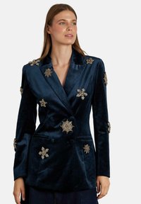 Donkerblauwe fluwelen blazer met metallic gouden en zilveren stervormige versieringen en dubbelgeknoopte knopen, met een gladde textuur.