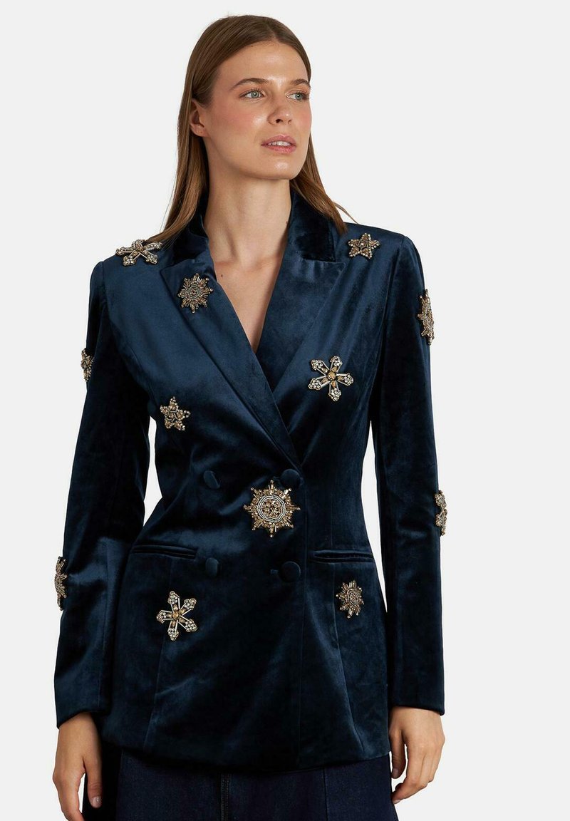 Donkerblauwe fluwelen blazer met metallic gouden en zilveren stervormige versieringen en dubbelgeknoopte knopen, met een gladde textuur.