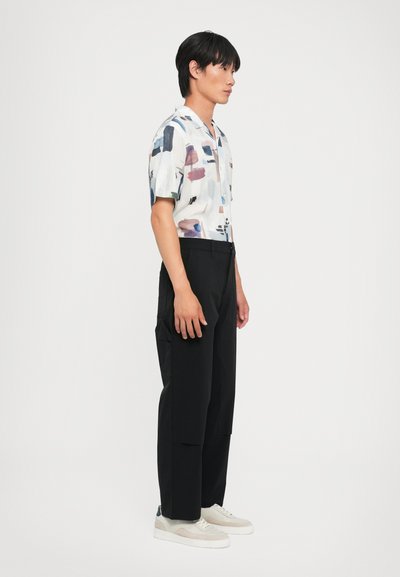 Camisa de manga corta con un patrón abstracto en colores pastel, combinada con pantalones anchos negros y zapatillas ligeras. Textura de tela suave.