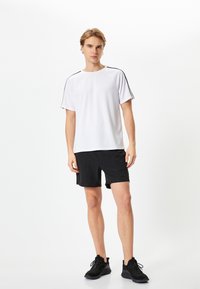 Hvid atletisk t-shirt med sorte sidestriber, parret med sorte shorts og sorte sneakers. Teksturstof; afslappet pasform.