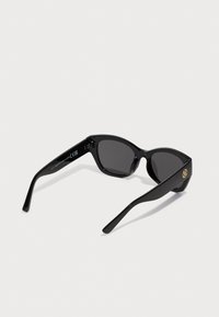 Schwarze Sonnenbrille mit einem Katzenaugen-Rahmen, dunklen Gläsern, glattem Kunststoffmaterial und goldenem Logo-Akzent am Bügel.