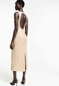 Shimmery gold midi dress with a back cutout, textured sequins, and a side slit. Adjusted fit accentuates the body's shape.
