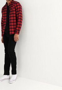 Camisa de franela a cuadros rojos y negros, pantalones negros y zapatillas blancas. Vista desde el suelo, con enfoque en el patrón de la tela y el ajuste.