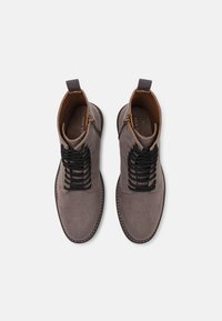 Botas de tobillo de ante gris con cordones negros, punta redonda y acentos marrones en contraste en el cuello y la suela. Cuenta con una lengüeta.