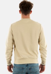 Sudadera beige con cuello redondo, puños y dobladillo de canalé. Tejido suave, diseño liso, vista trasera sin logotipos ni patrones adicionales.