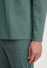 Langsleevige, effen groene top van zachte stof, gecombineerd met gemêleerde groene en blauwe leggings met geometrische ontwerpen.