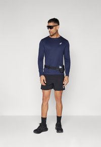 Marine langærmet skjorte, sorte shorts, sorte sko og solbriller. Inkluderer et taljebælte med en holder til vandflaske for bekvemmelighed.