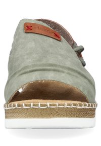 Espadrille en daim vert avec une étiquette en cuir beige, design ouvert à l'avant, semelle en jute brun clair et accents en caoutchouc blanc. Forme ronde et texture douce.