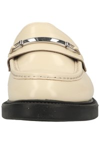 Mocassin en cuir beige avec une semelle noire et un détail barre métallique argentée sur le dessus, présenté de face.