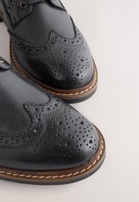 Schwarze Brogue-Lederschuhe mit dekorativen Perforationen, braunen Nähten und einer runden Spitze. Verfügen über eine robuste Sohle für Langlebigkeit.
