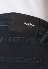 Dark blue denim jeans with a black leather patch featuring white "Pepe Jeans London" branding, detailed stitching, and a metal button.