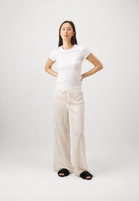 Vit kortärmad skjorta tillsammans med ljusbeige vida byxor med elastisk midja och snöre. Svarta fluffiga tofflor fulländar outfiten.