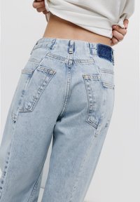 Lichtblauwe denim jeans met een hoge taille, voorzien van een blauwe accent aan de tailleband en twee achterzakken met een vervaagde textuur.