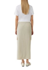 Beige maxi skirt with side pockets, smooth texture, and subtle stitching details, worn with a short-sleeved white t-shirt and light shoes.